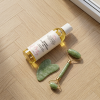 Glimmer Goddess organic facial massage oil, jade roller, and Gua Sha stone laid flat on light oak parquet floor