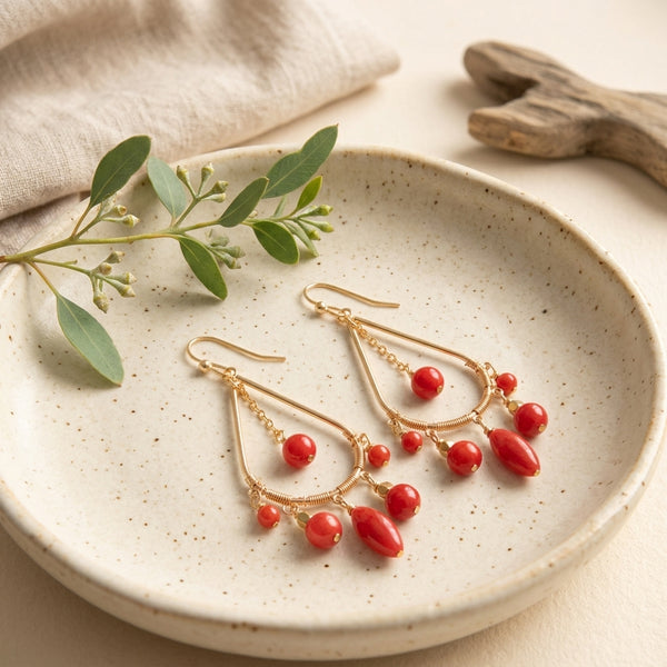 Red Jade Chandelier Earrings with golden bronze wire work resting on a speckled cream ceramic dish next to a green branch